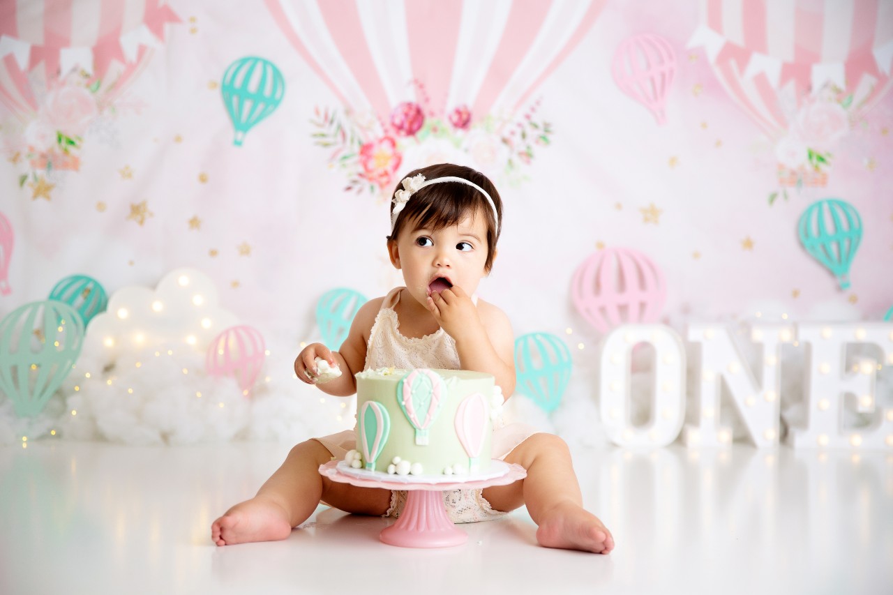 Baby sitting in front of a cake and lots of decorations with a big smile